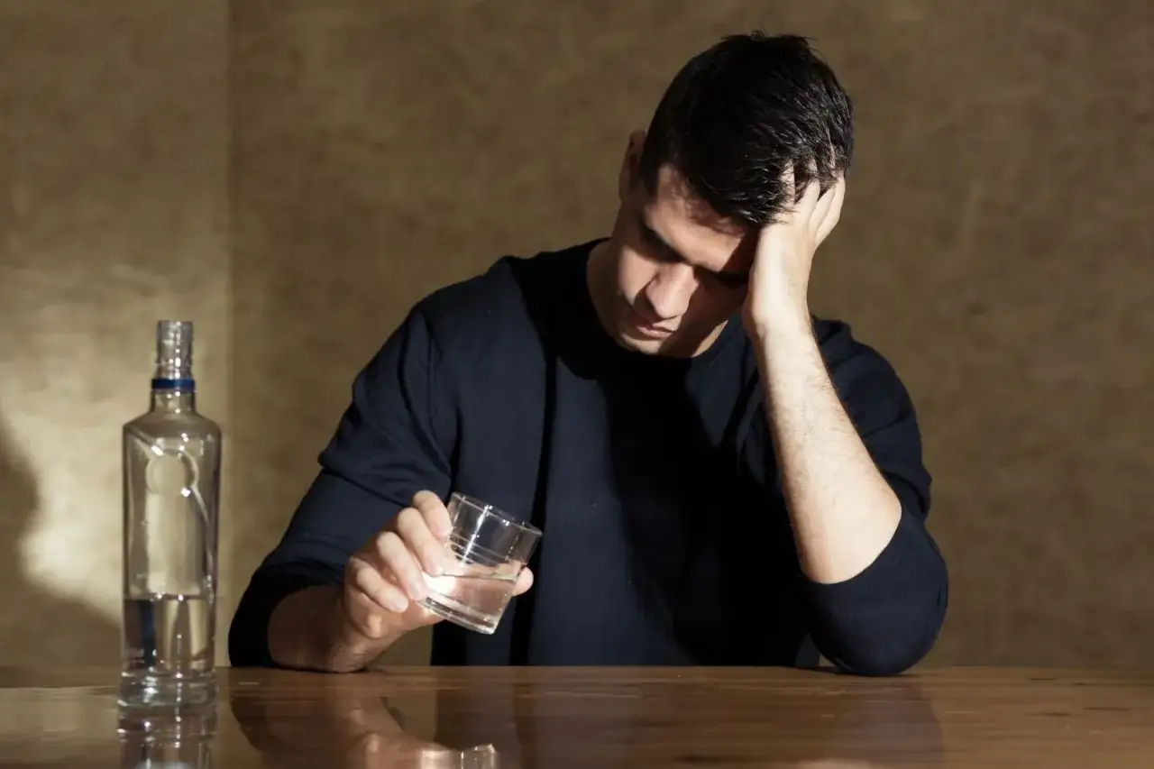 Mężczyzna z butelką alkoholu i szklanką, zamyślony. Pamiętaj, z czym nie łączyć antydepresantów.
