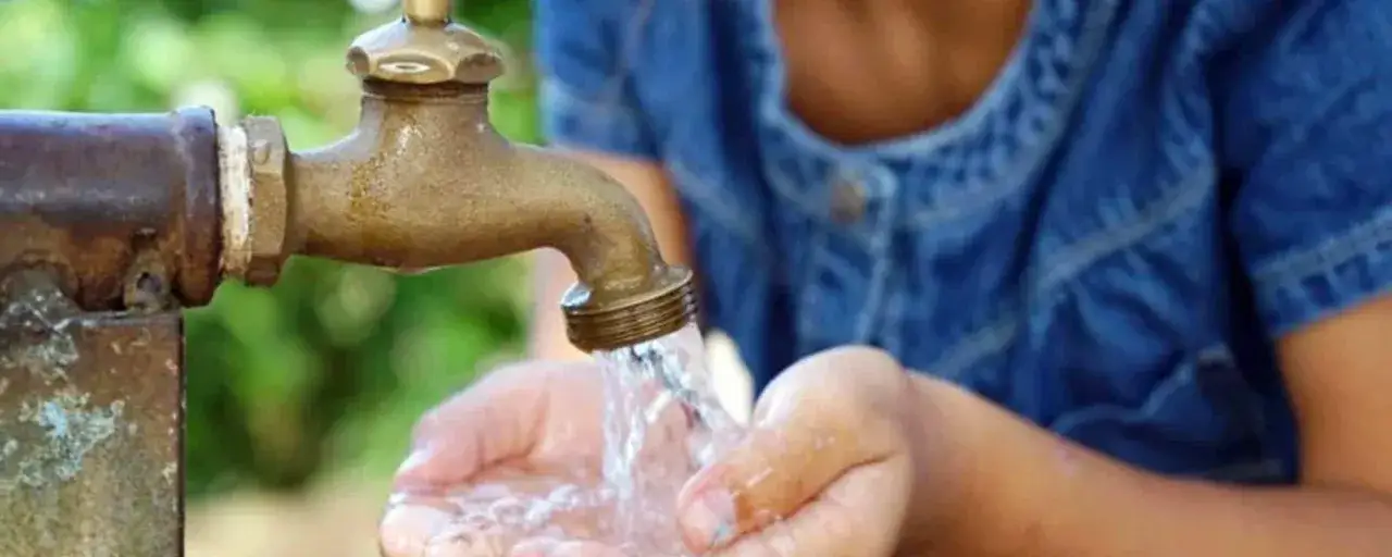 Niño recibe agua de un grifo antiguo, un gesto que resalta la importancia de la calidad del agua para la vida.