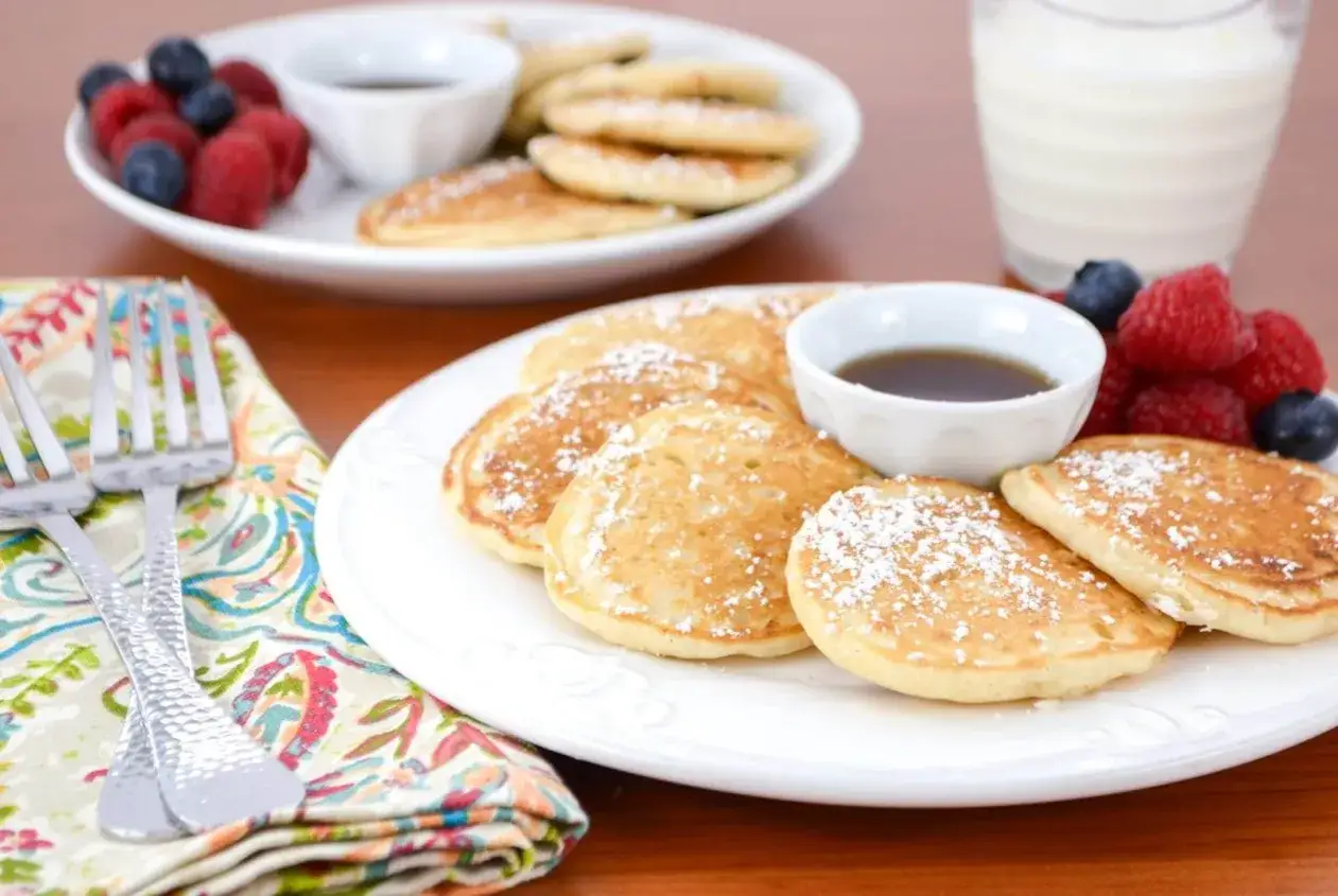 Kleine Dinkel Pancakes, best&auml;ubt mit Puderzucker, serviert mit Beeren und Ahornsirup. Ein k&ouml;stliches Fr&uuml;hst&uuml;ck!