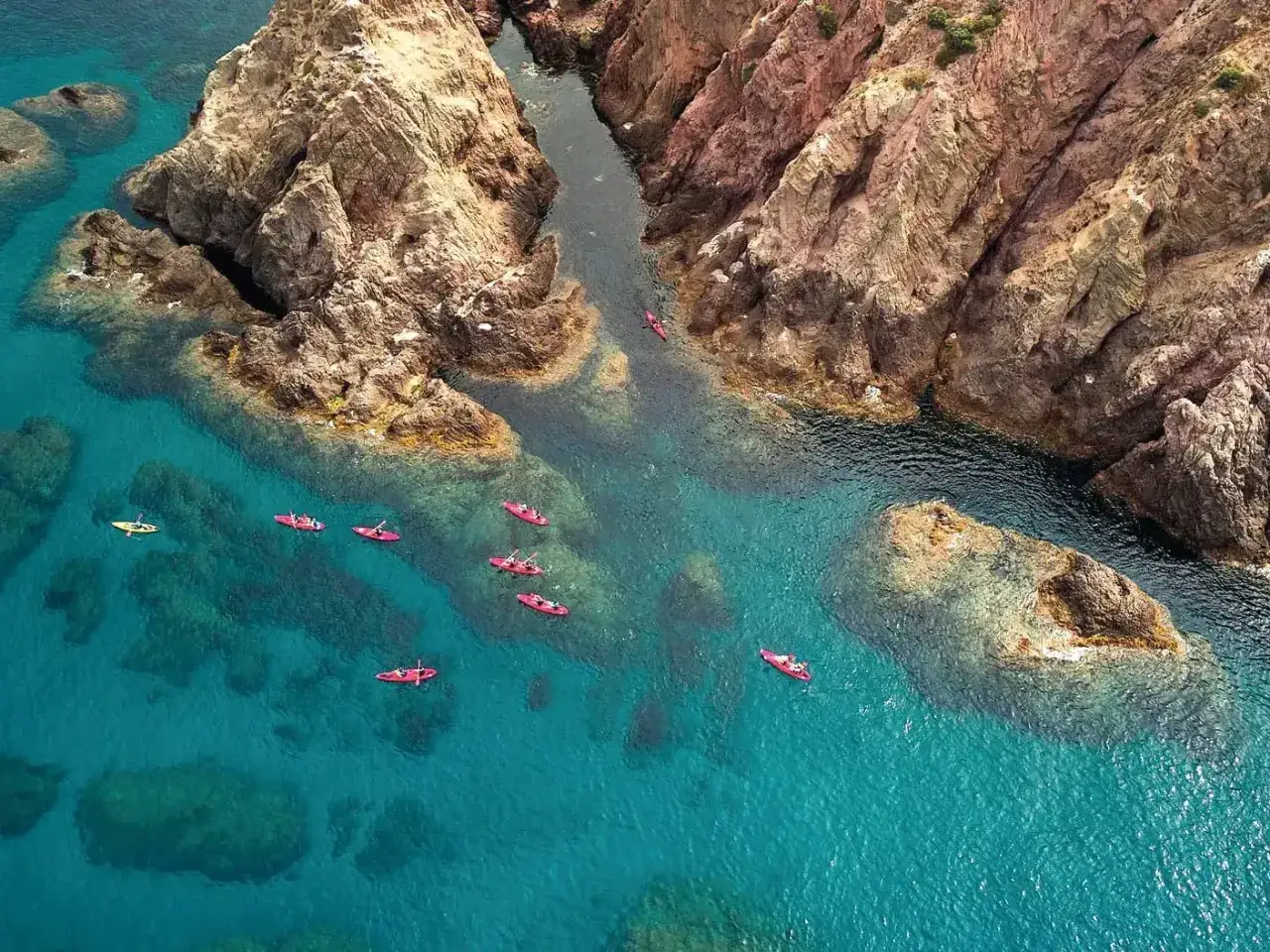 Kayaks navegan por aguas turquesas cerca de acantilados rocosos, explorando la **playa de las amoladeras**.