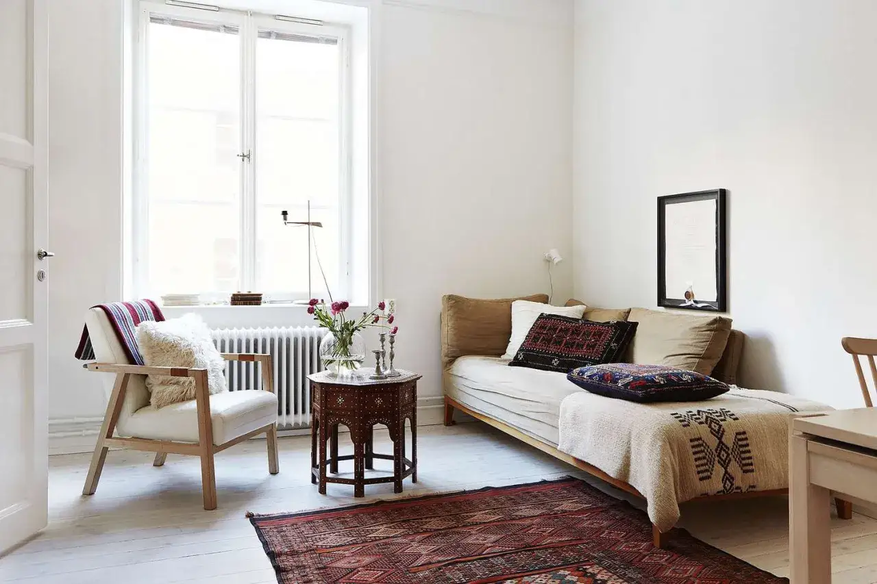 Ideas para decorar un piso pequeño con poco dinero: sillón blanco, sofá cama, mesa auxiliar marroquí, alfombra oriental y cojines étnicos.
