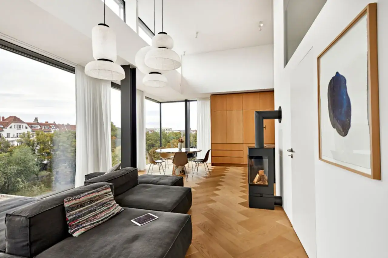 Gemütliches Wohnzimmer mit einem dunklen Sofa vor bodentiefen Fenstern, die viel Licht hereinlassen. Ein Kamin sorgt für Wärme.