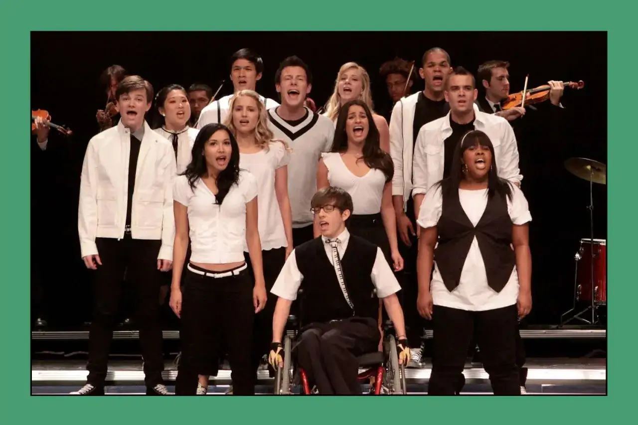 Ensemblen från Glee sjunger unisont. En violinist spelar i bakgrunden.