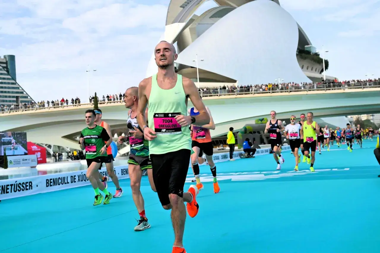 Biegacze na trasie maratonu w Walencji, z nowoczesną architekturą w tle.