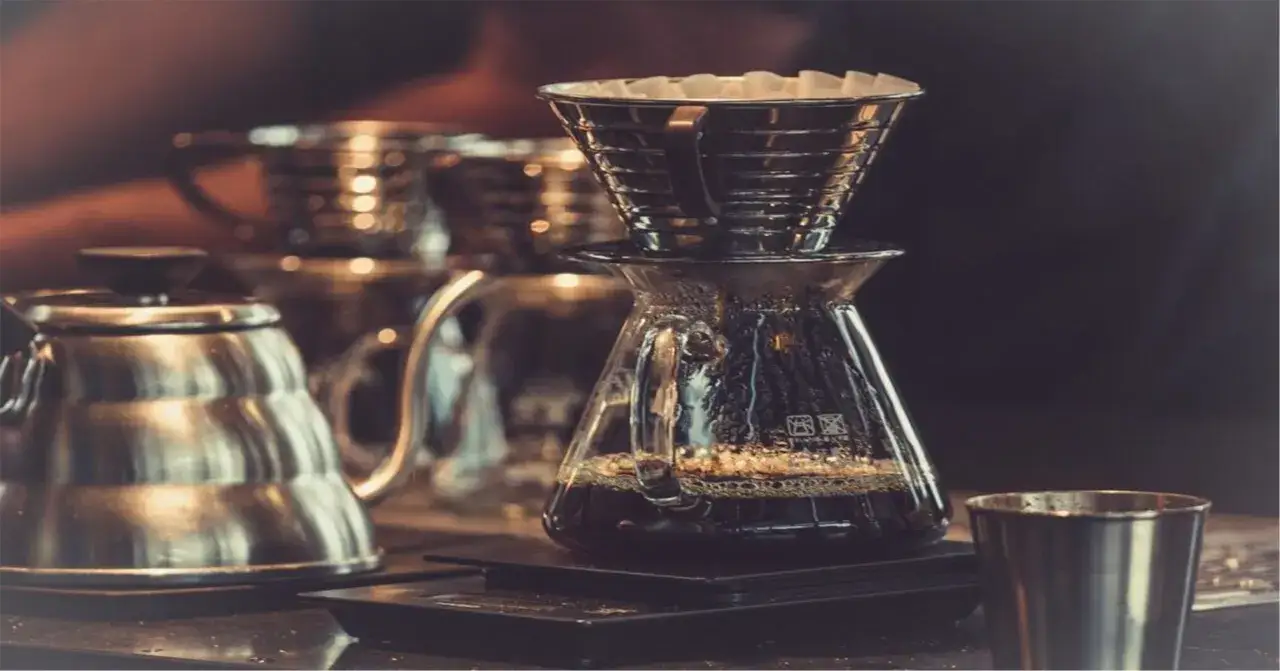 En kaffebryggare med filter och en kanna fylld med färskt kaffe. En del av en vattenkokare syns till vänster. En perfekt start för din kaffe guide.