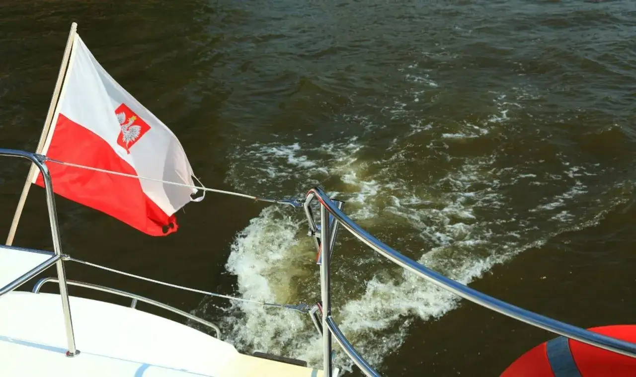 Flaga bandery w Polsce dumnie powiewa na rufie statku, gdy ten pruje fale.