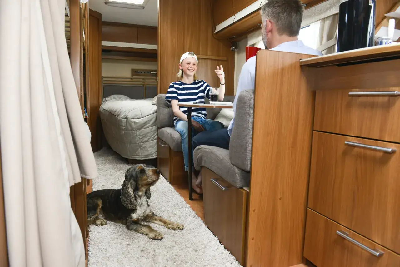 Un enfant et un homme discutent dans un camping-car, un chien est couch&eacute; sur le tapis. Une astuce chauffage camping-car pour un voyage confortable.