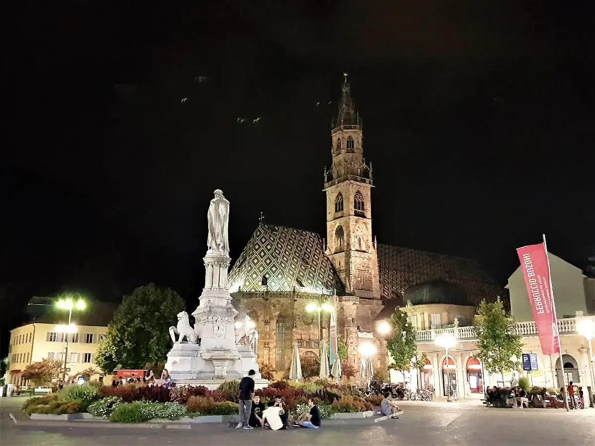 Piazza Walther di Bolzano di notte, con il Duomo illuminato e il monumento a Walther von der Vogelweide. Un'atmosfera magica per scoprire Bolzano in un giorno.