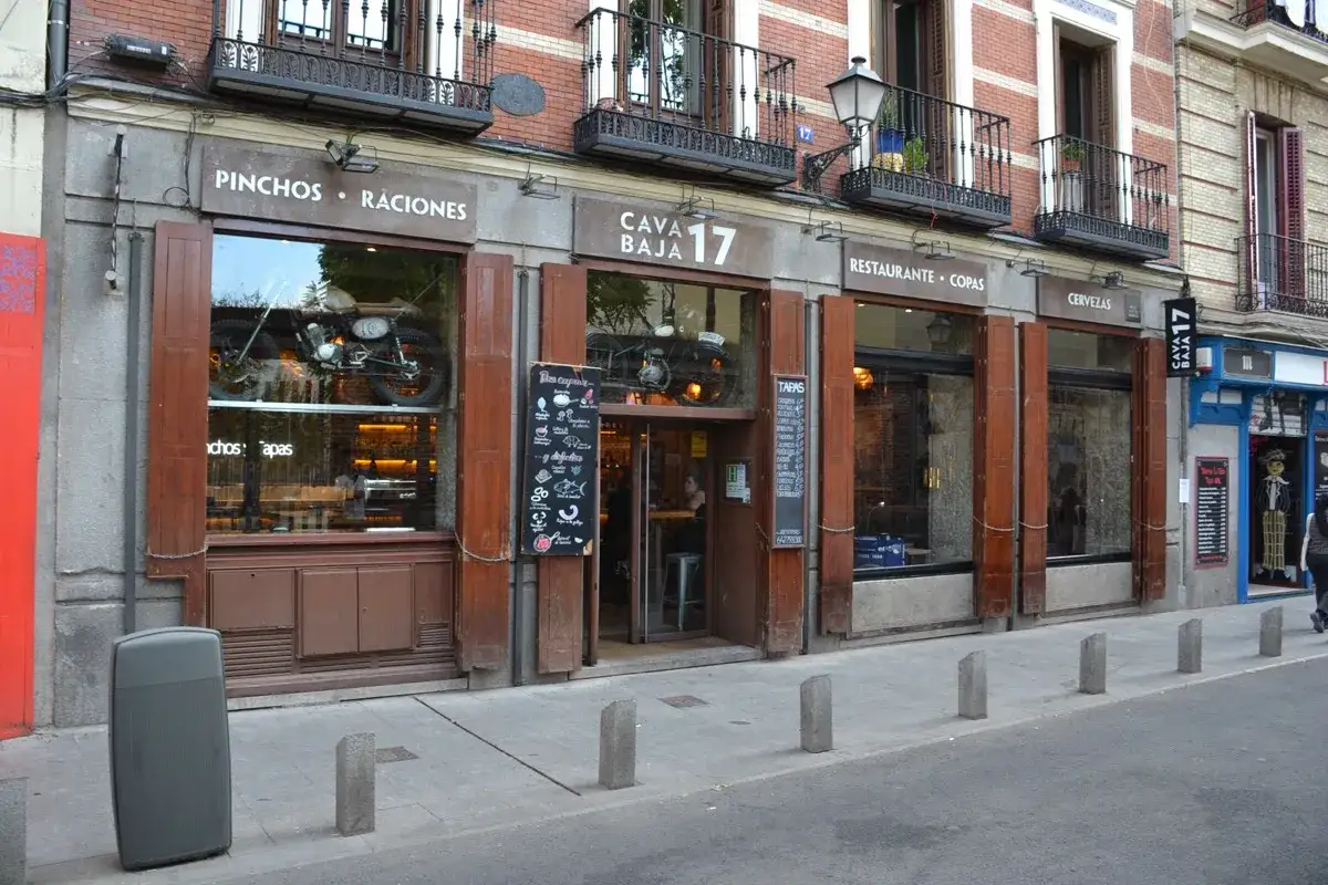 Fachada del restaurante Cava Baja 17, con una moto vintage en el escaparate y menús de tapas y raciones.