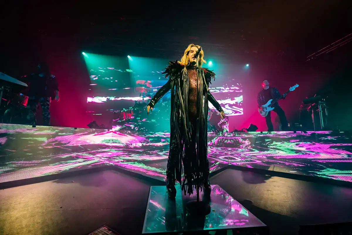 Bill Kaulitz z Tokio Hotel Polska w spektakularnej kreacji na scenie, otoczony kolorowymi światłami i wizualizacjami.