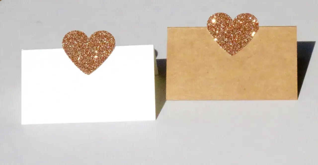 Segnaposto nozze d'oro fai da te: due cartoncini, uno bianco e uno kraft, decorati con cuori glitterati color oro.