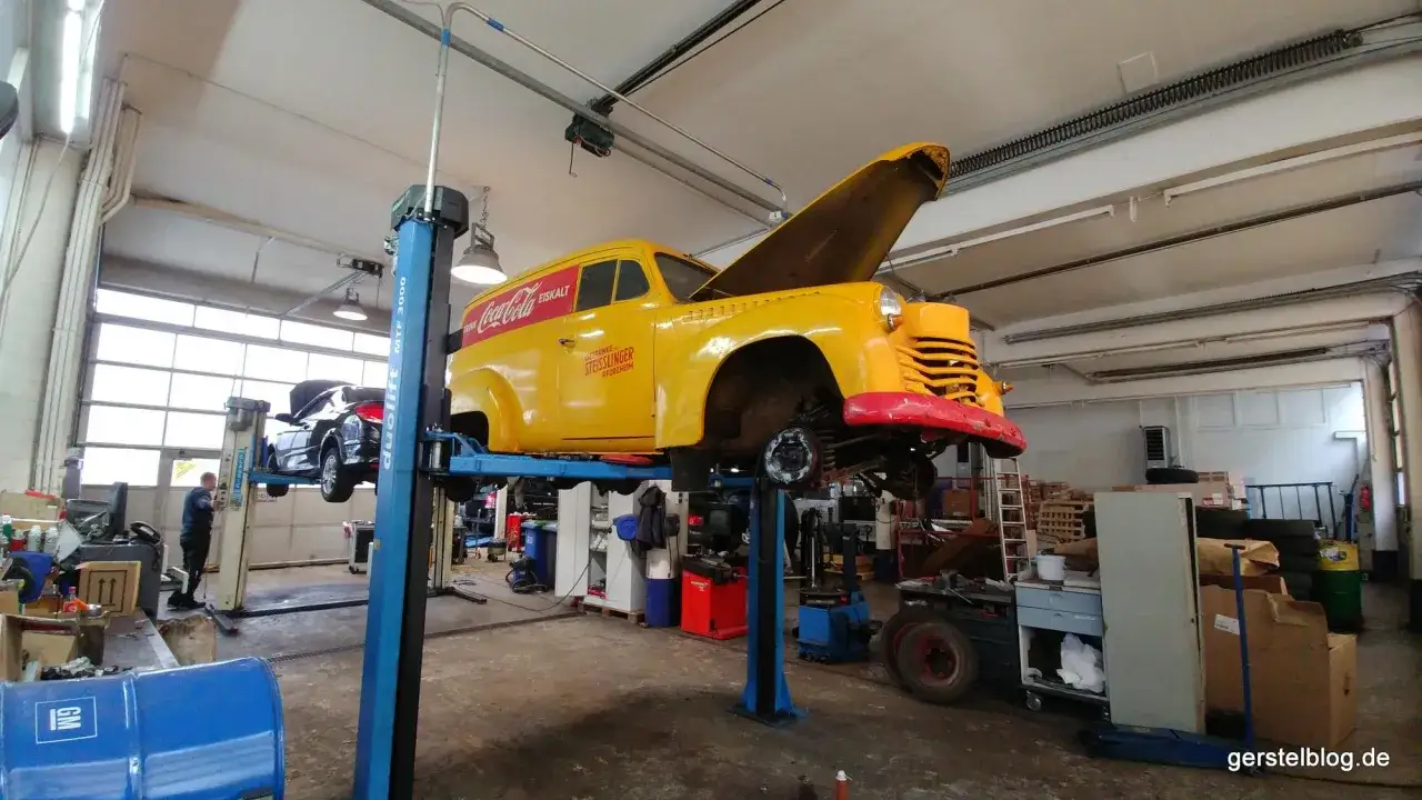 Gelber Oldtimer mit Coca-Cola-Werbung auf Hebebühne, bereit für die Oldtimer Restauration.