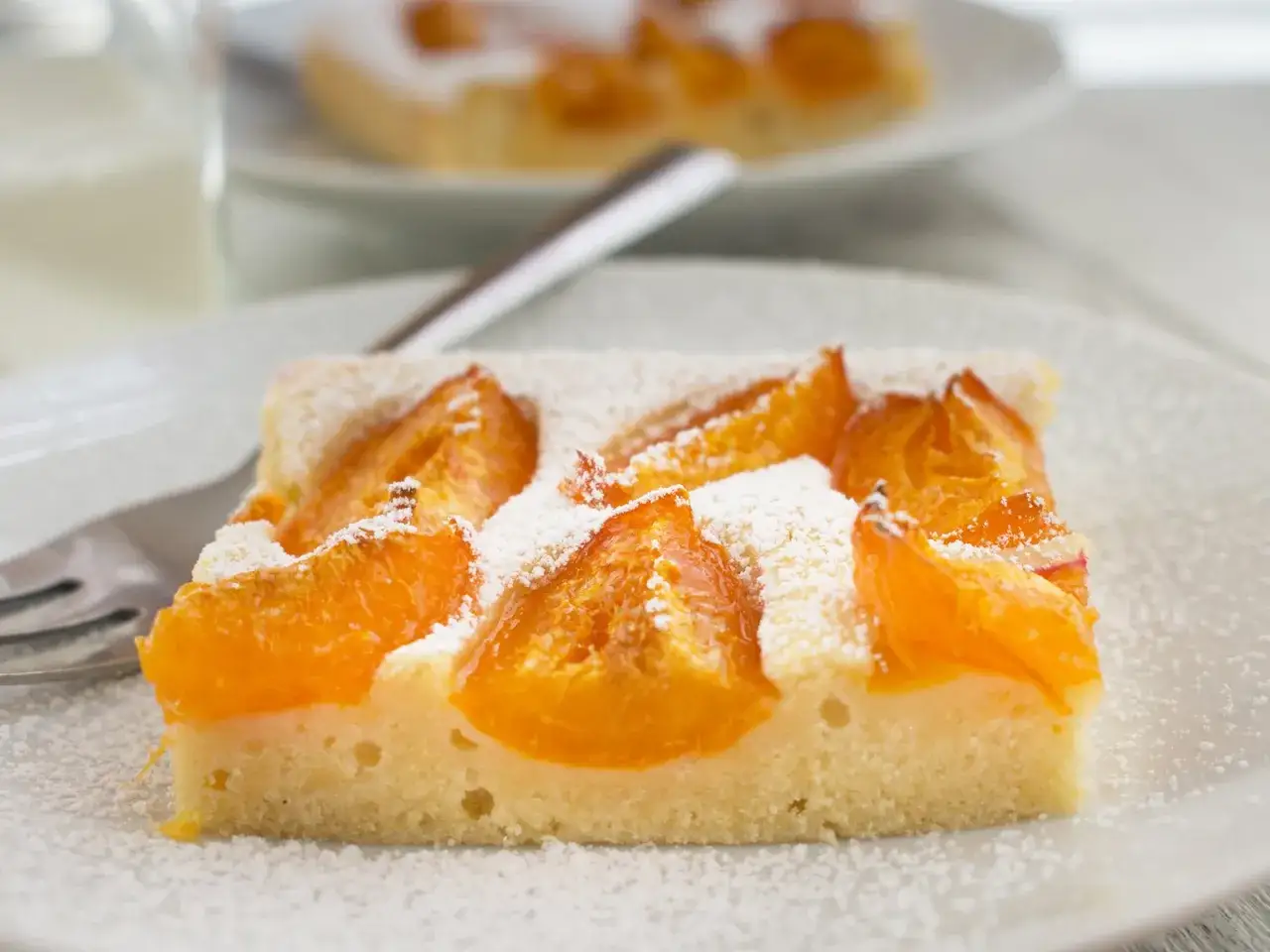 Saftiges Stück Aprikosenkuchen, bestäubt mit Puderzucker. Ein köstliches Aprikosenkuchen Rezept für den Sommer.