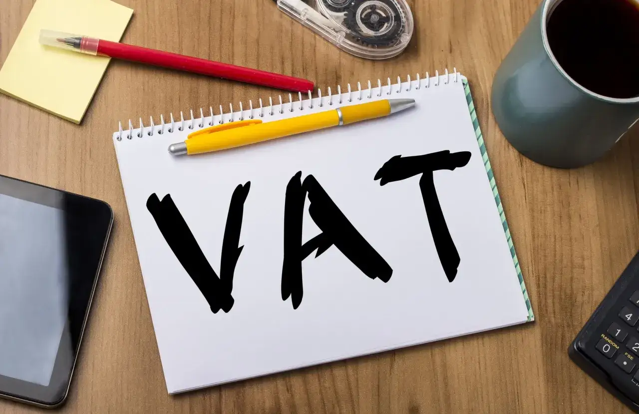 Notatnik z napisem VAT, obok tablet, długopisy, kubek kawy i kalkulator. Czas na rozliczenie **wnt obowiązek podatkowy**.