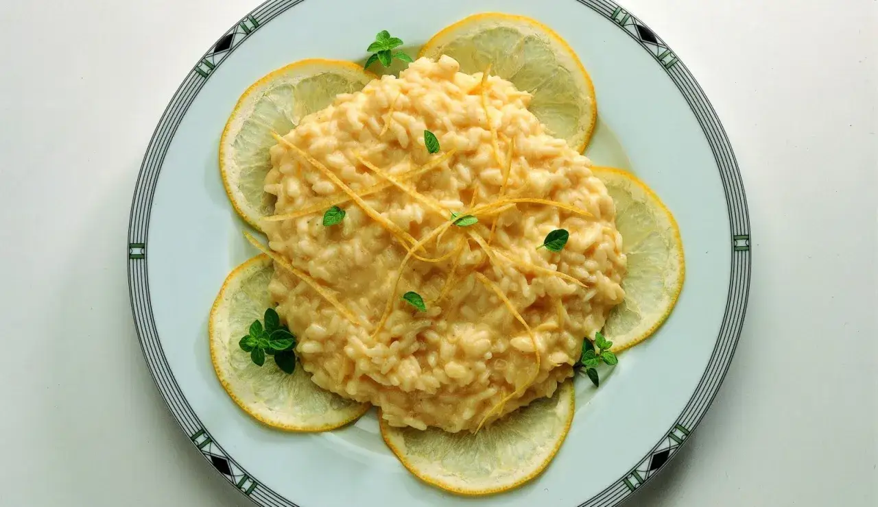 Un cremoso risotto al limone gourmet, guarnito con scorzette di limone e foglioline verdi, circondato da fette di limone fresco su un piatto elegante.
