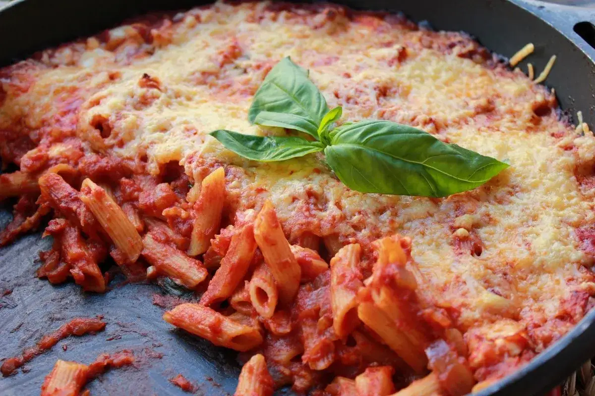 Macarrones al horno cubiertos de queso derretido y salsa de tomate, decorados con una hoja de albahaca fresca. &iexcl;Un plato casero irresistible!