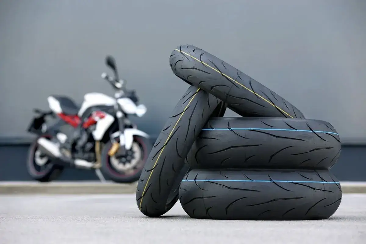 Stos nowych opon motocyklowych, gotowych do testu. W tle biało-czerwony motocykl.