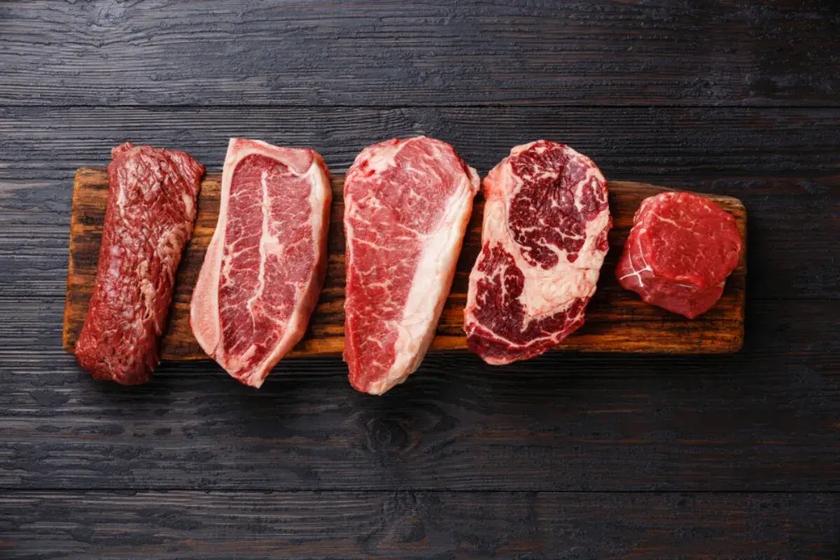 Pięć różnych rodzajów steków ułożonych na drewnianej desce: antrykot, rostbef, T-bone, ribeye i polędwica.