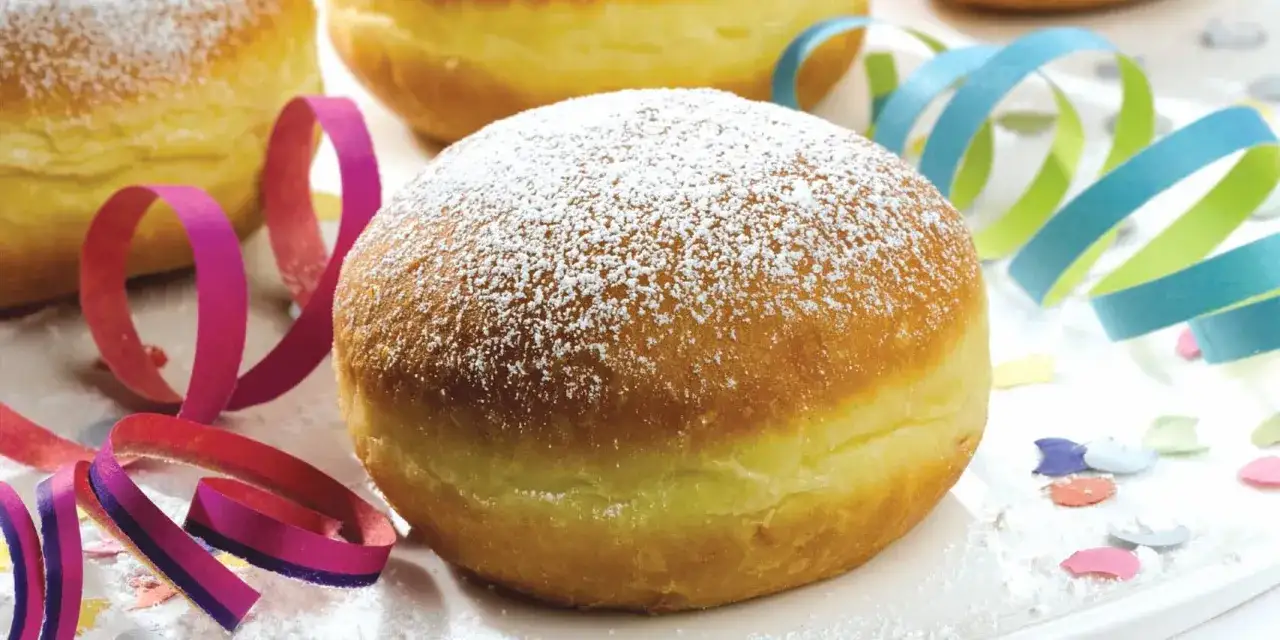 Frisch gebackene Faschingskrapfen, best&auml;ubt mit Puderzucker, liegen bereit f&uuml;r die n&auml;rrische Zeit. Bunte Luftschlangen und Konfetti machen Lust auf Fasching.