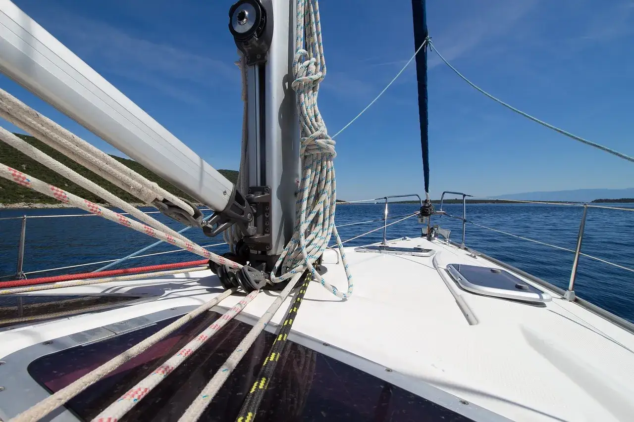 Vue de l'avant d'un voilier naviguant sur une mer bleue. Les cordages sont bien rangés, prêts pour le prochain hale bas.