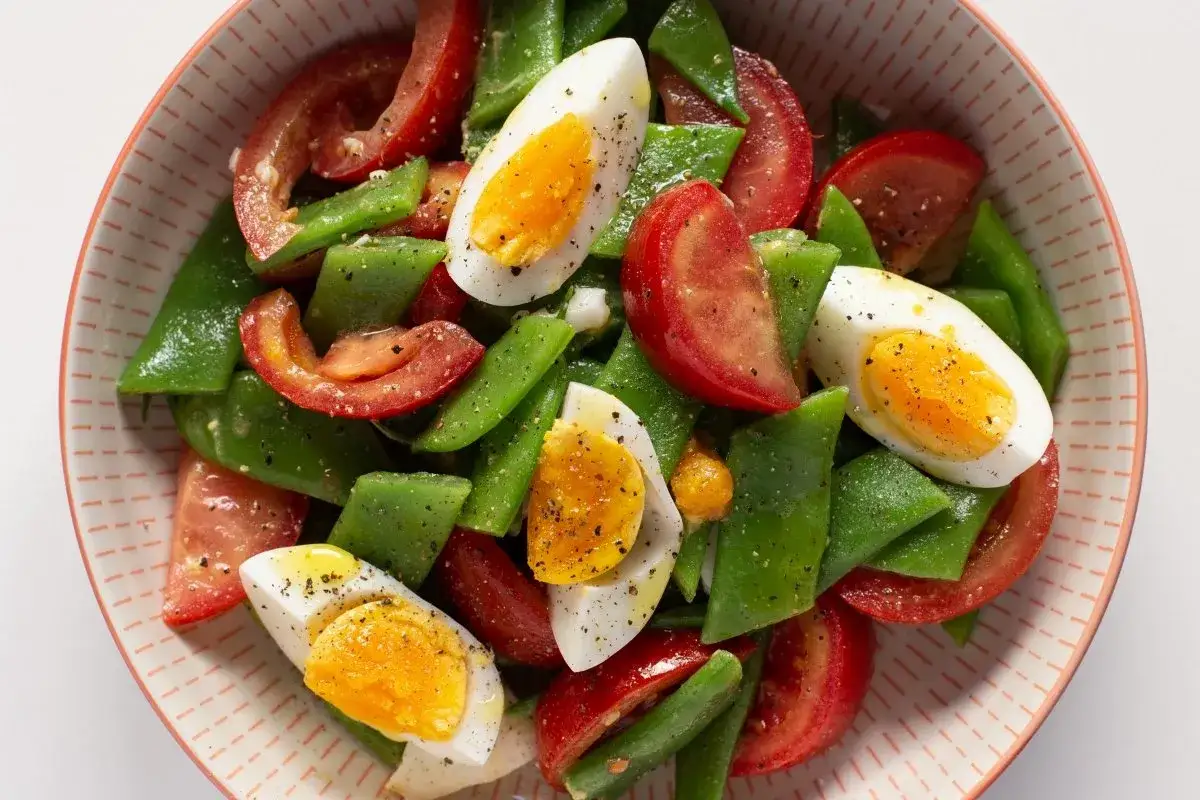 Ensalada fresca con judías verdes, tomates y huevos cocidos, aderezada con pimienta negra.