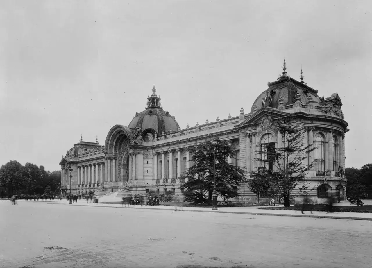 El Petit Palais, un majestuoso edificio con c&uacute;pulas y columnas, se alza imponente en un d&iacute;a nublado. Figuras borrosas pasean por la plaza.