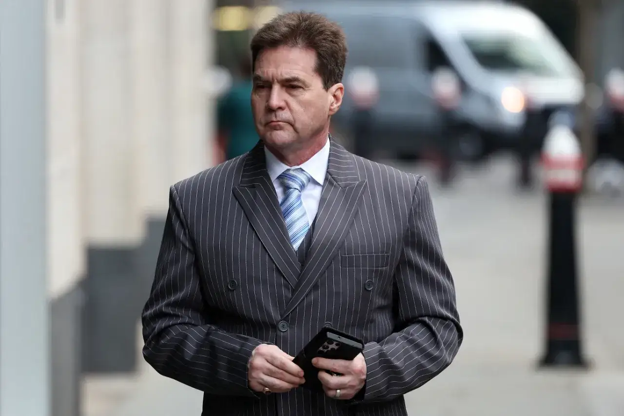 Craig Wright w garniturze w prążki, trzymający telefon, idzie ulicą.