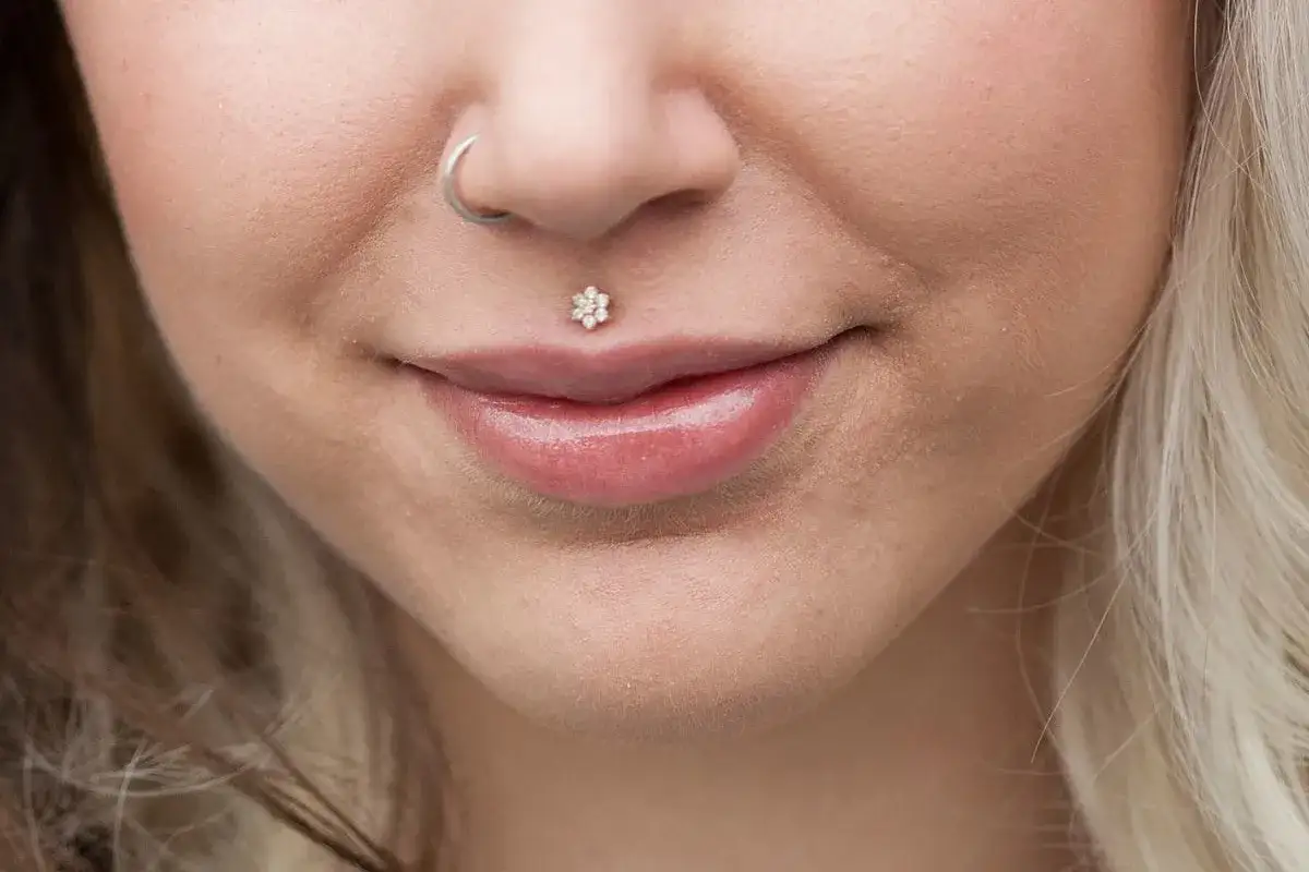 Usta z błyszczącym błyszczykiem i delikatnym kwiatowym medusa piercingiem. Kolczyk w nosie dodaje uroku.