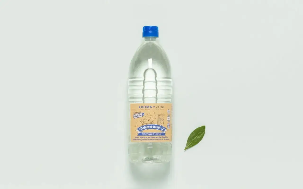 Bouteille de vinaigre d'alcool Aroma-Zone, un désinfectant naturel pour un nettoyage écologique. Une feuille verte à côté.