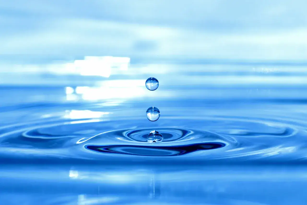 Wassertropfen f&auml;llt in ruhiges Wasser. Die Frage, ob Polyester wasserdicht ist, bleibt offen, aber diese Tropfen zeigen die reine Form von Wasser.