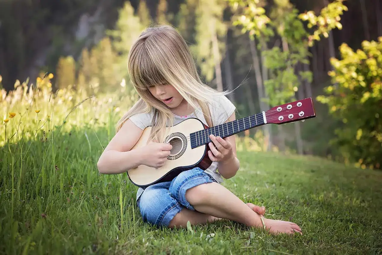 Dziewczynka gra na gitarze w trawie, ucząc się prostych piosenek na gitarę dla dzieci.