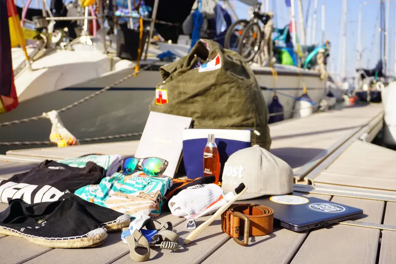 Packliste Segeln: Kleidung, Sonnenbrille, Buch, Zahnbürste, Gürtel, Laptop und eine Tasche. Alles bereit für die Reise!