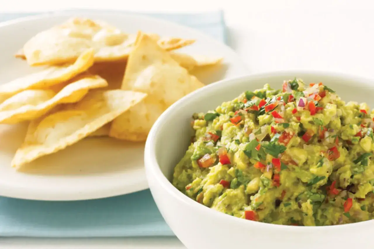 En sk&aring;l med kr&auml;mig guacamole, toppad med finhackad chili och koriander, bredvid en h&ouml;g med tortillachips. Perfekt f&ouml;r ett enkelt guacamole recept.