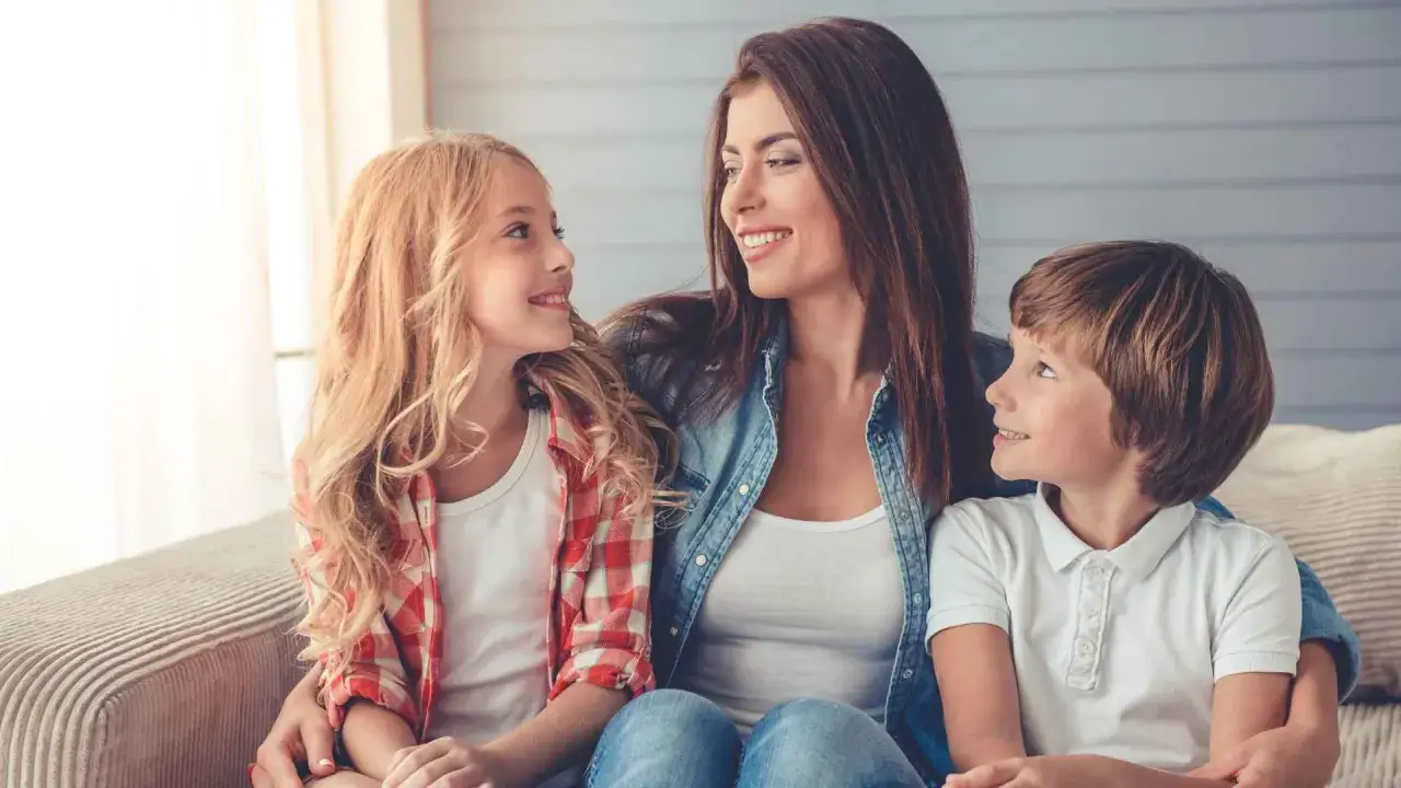 Glückliche alleinerziehende Mutter mit 2 Kindern, die sich liebevoll ansehen. Sie fragt sich, was ihr zusteht.