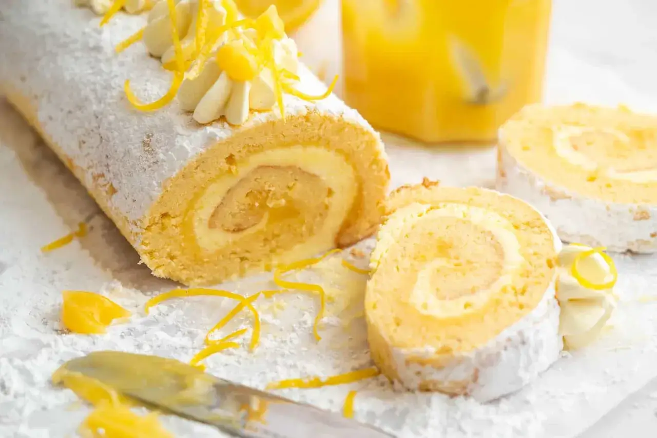 En härlig glutenfri rulltårta med citronsmak, pudrad med florsocker och garnerad med grädde och citronskal.