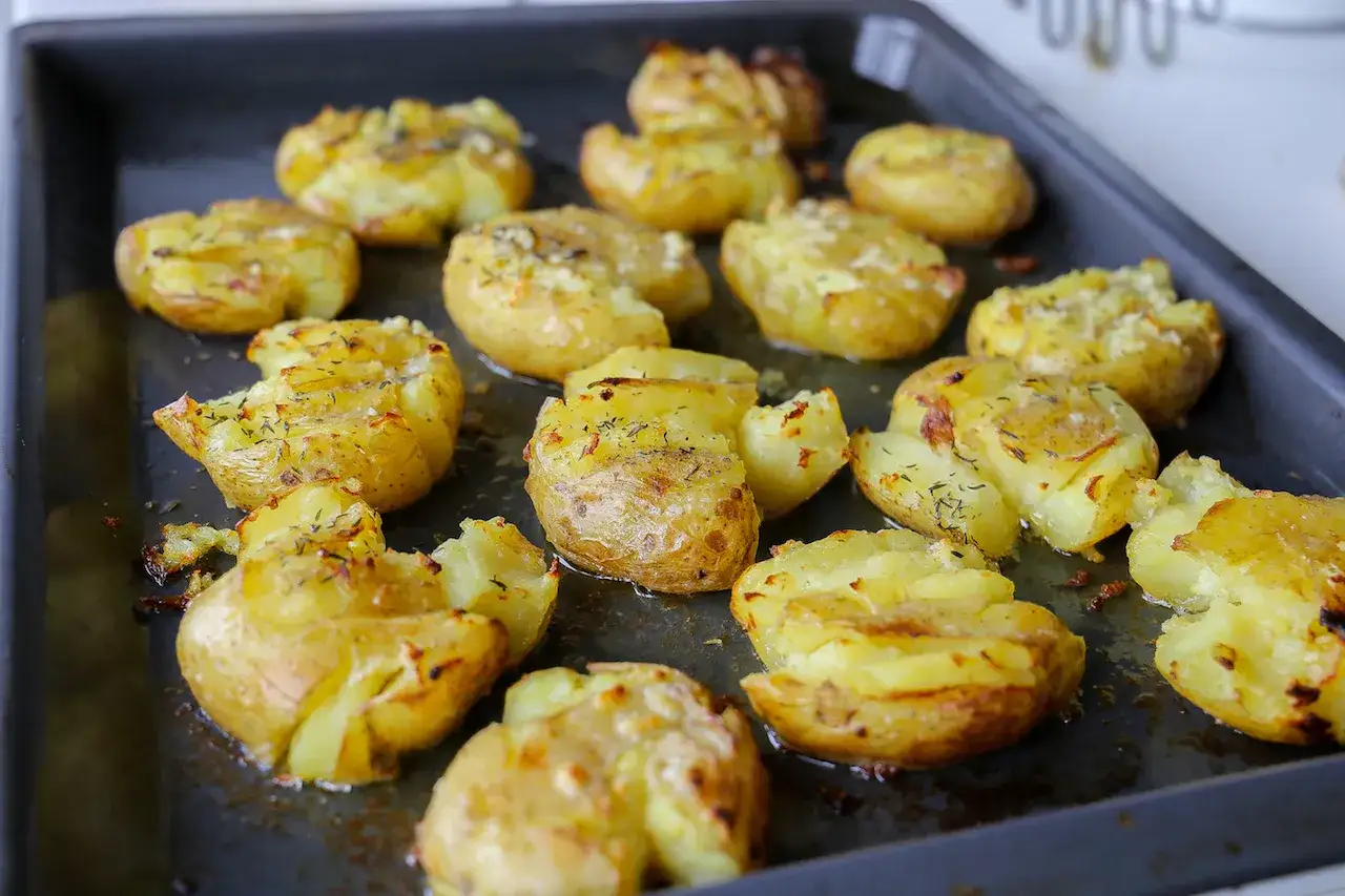 Ugnsbakade smashed potatoes med ost och &ouml;rter p&aring; en pl&aring;t. Krispiga och gyllene, redo att serveras.