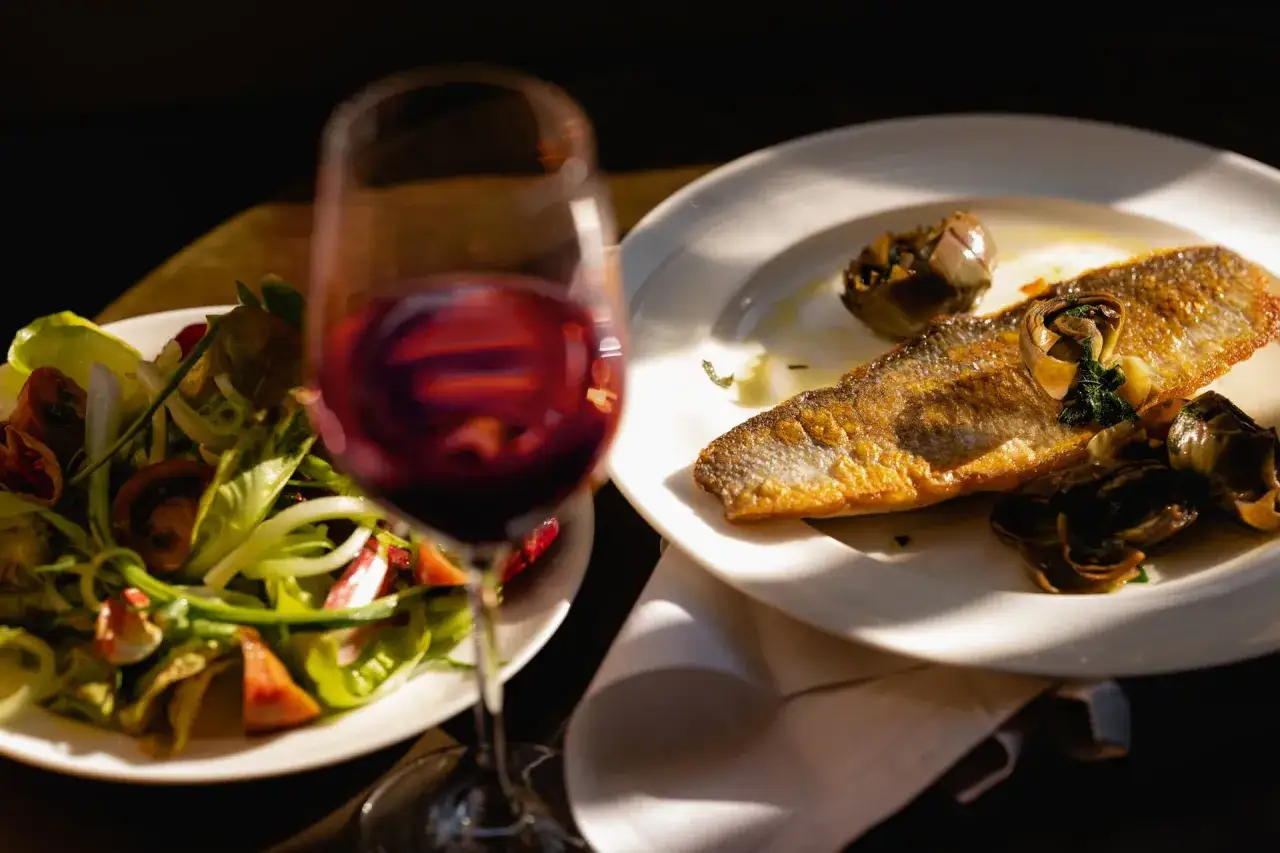 Un verre de vin rouge accompagne un d&eacute;licieux poisson grill&eacute; et une salade fra&icirc;che.