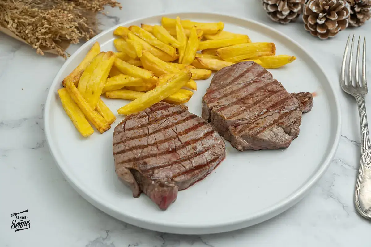 Dos jugosos solomillos a la plancha con marcas de parrilla, acompa&ntilde;ados de patatas fritas doradas. Un plato cl&aacute;sico y delicioso.