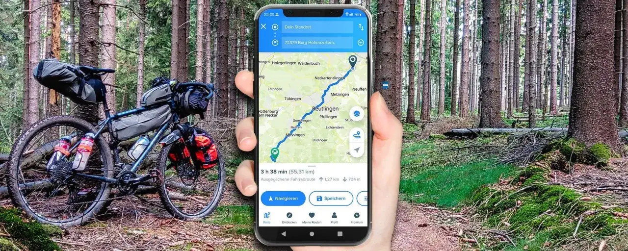 Rower trekkingowy w lesie, a w dłoni smartfon z aplikacją na rower pokazującą trasę.