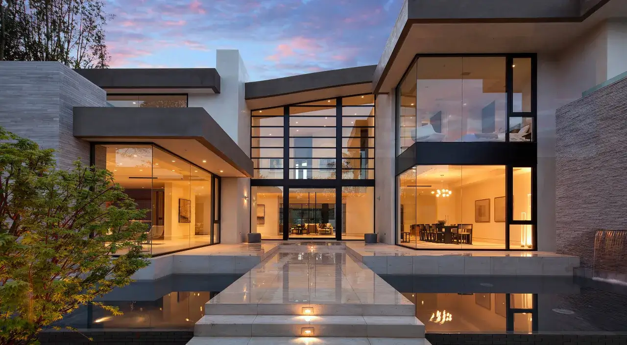 Casa moderna con amplios ventanales que reflejan el cielo crepuscular. Los cristales guardian sun capturan la luz, creando un ambiente c&aacute;lido y acogedor.