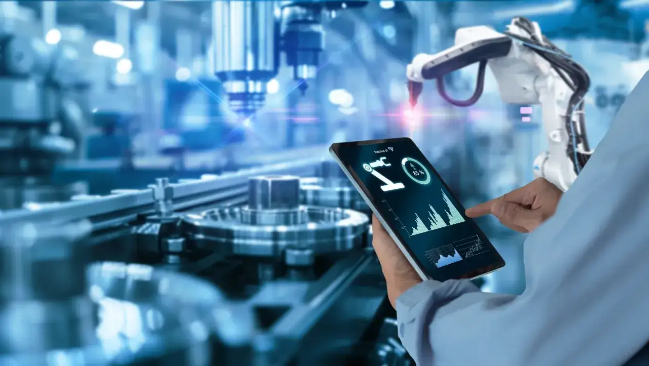 Operator kontroluje pracę robota przemysłowego za pomocą tabletu, na którym widnieje wykres i wskaźnik obciążenia, sugerujący działanie czujnika siły.