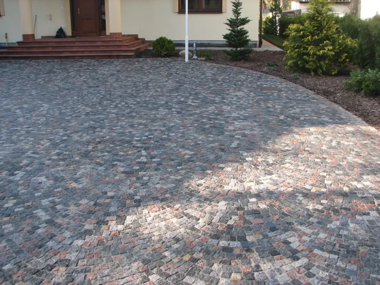 Podjazd z kostki granitowej ułożonej w łuk. Widać schody i fragment domu. Szacunkowo ok. 100 kostki granitowej na m2.