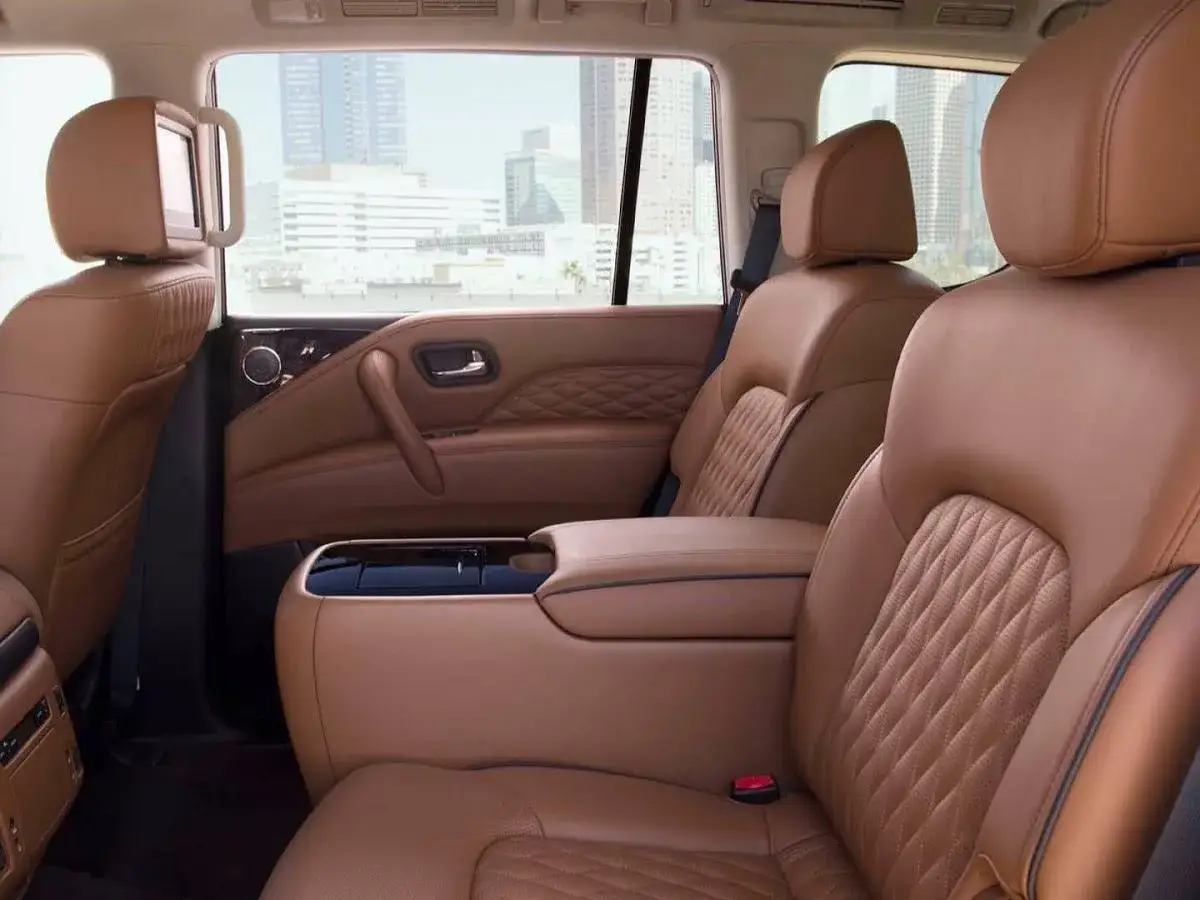 Wnętrze Infiniti QX80 z brązową, pikowaną skórą, ekranem multimedialnym i widokiem na miasto.