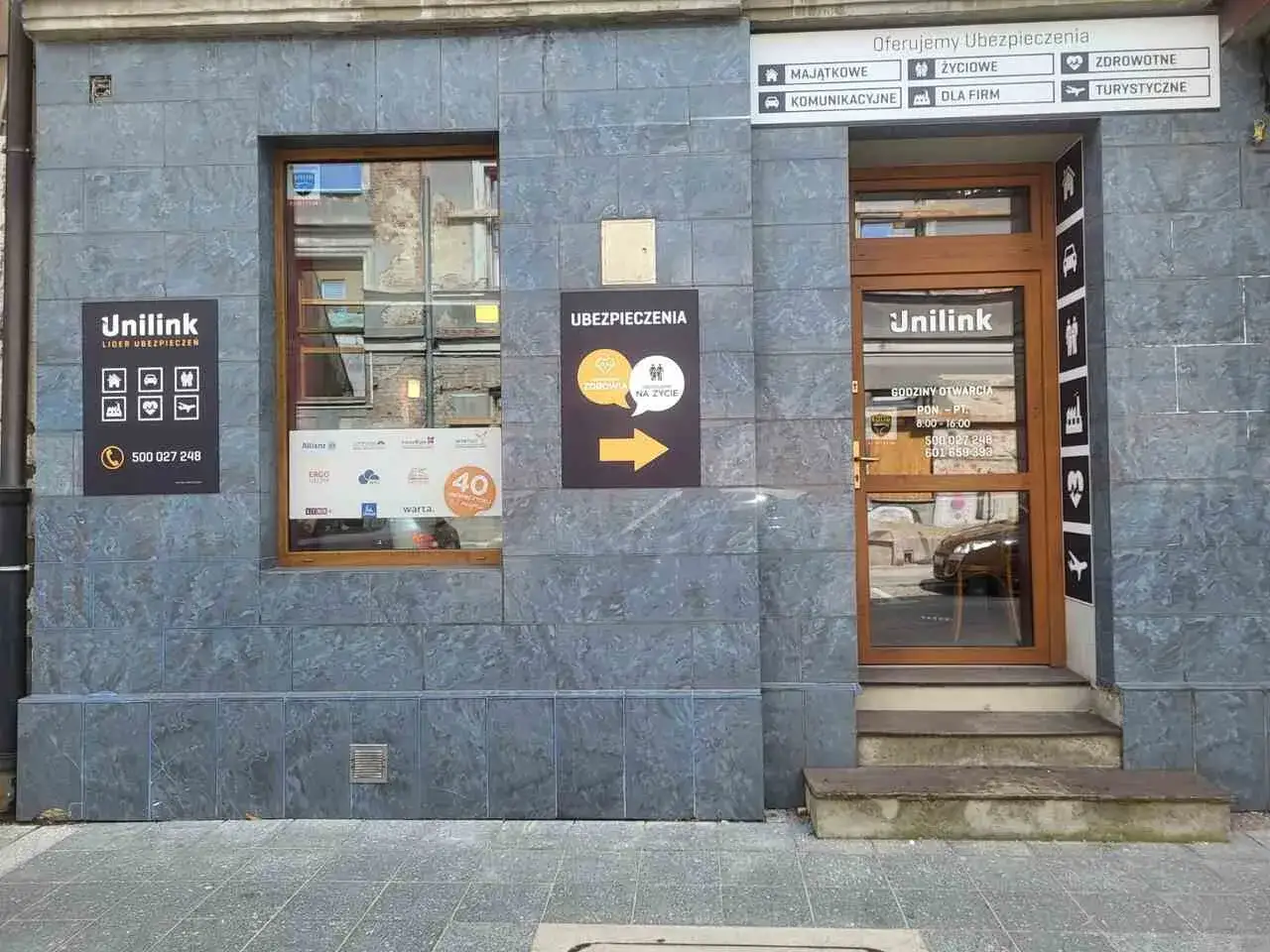 Elewacja biura Unilink z drzwiami i oknem, na ścianie tablice informacyjne o ubezpieczeniach.