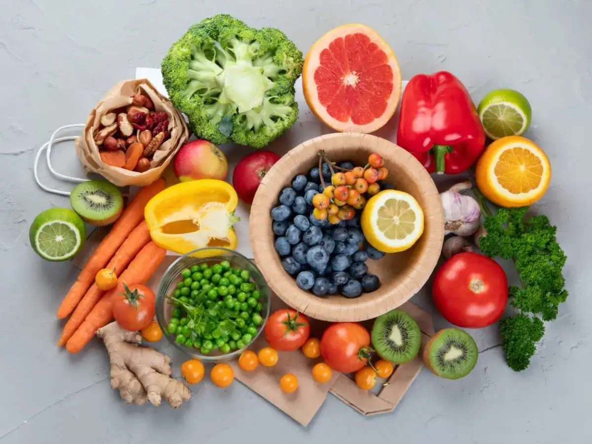Bunte Fr&uuml;chte und Gem&uuml;se wie Beeren, Zitrusfr&uuml;chte, Paprika und Brokkoli, reich an Vitamin C, liegen auf einem grauen Untergrund.