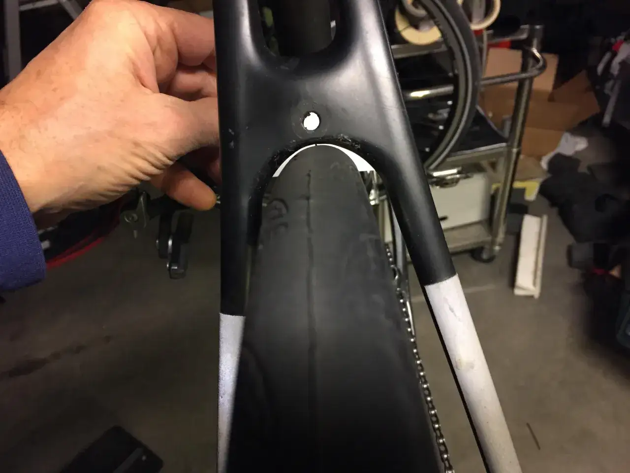 A hand is checking the clearance between a road bike's frame and a wide tire, possibly a mountain bike tire.