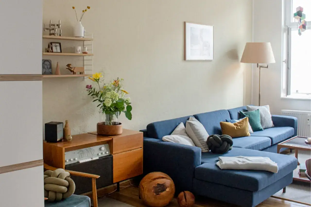 Ein gem&uuml;tliches Wohnzimmer mit einem tiefblauen Ecksofa, das mit Kissen in verschiedenen Farben und Mustern dekoriert ist. Was passt zu blau? Warme Holzt&ouml;ne und erdige Akzente.