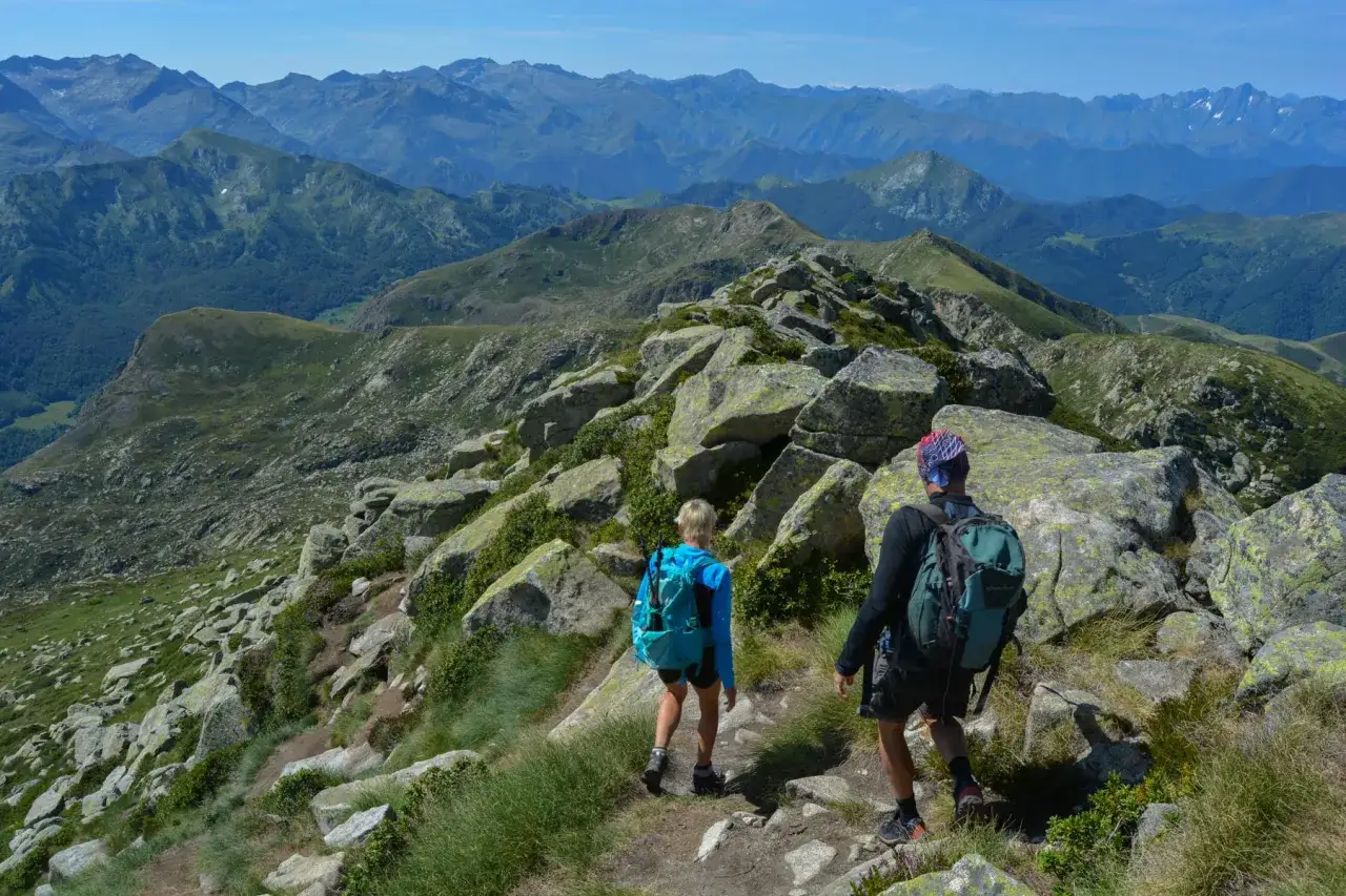 Deux randonneurs escaladent un sentier rocheux vers le pic des 3 Seigneurs, offrant une vue panoramique sur les Pyrénées verdoyantes.