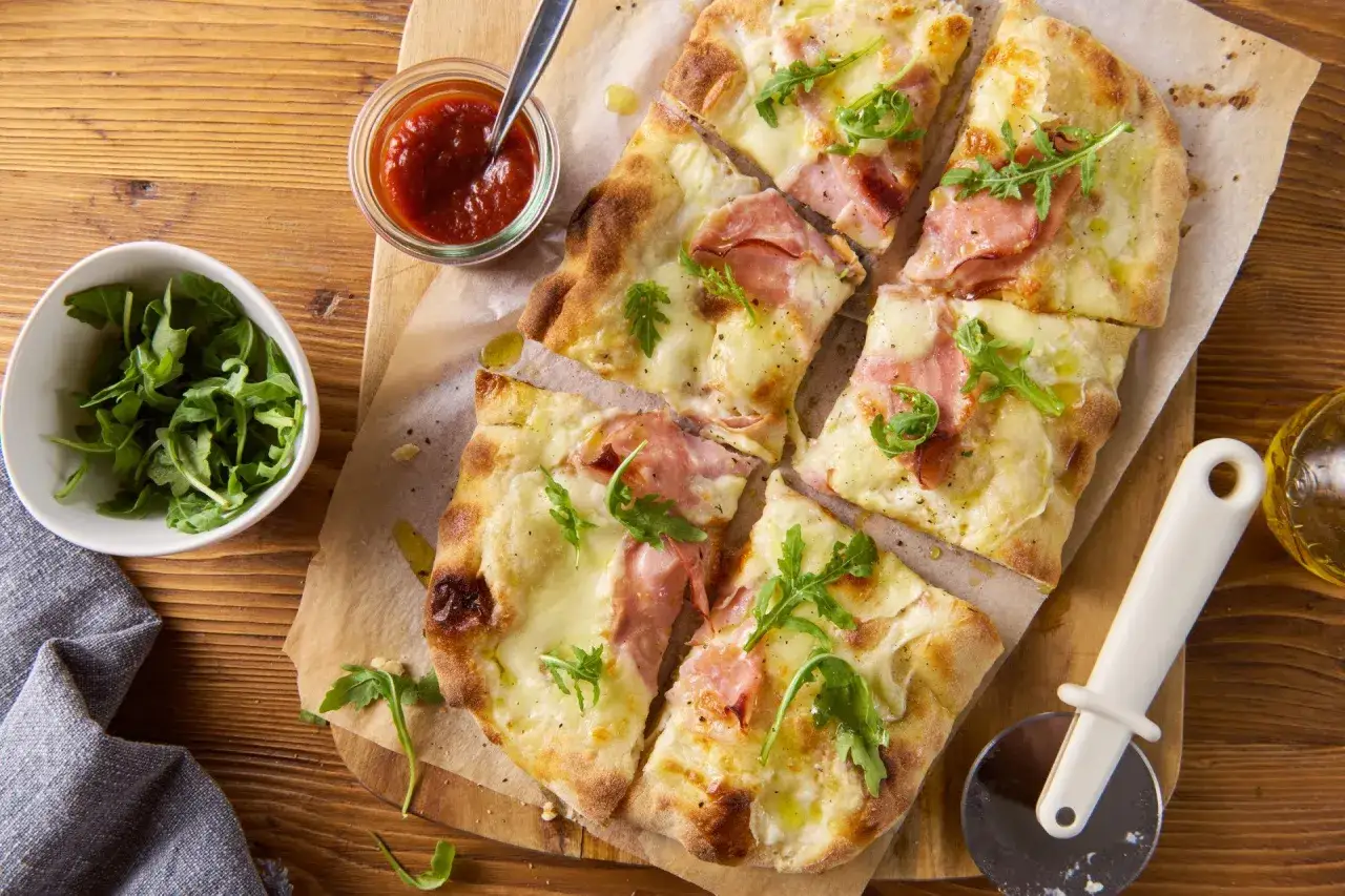 Pizza bianca z szynką i rukolą, podana z sosem pomidorowym. Idealna na szybki obiad.