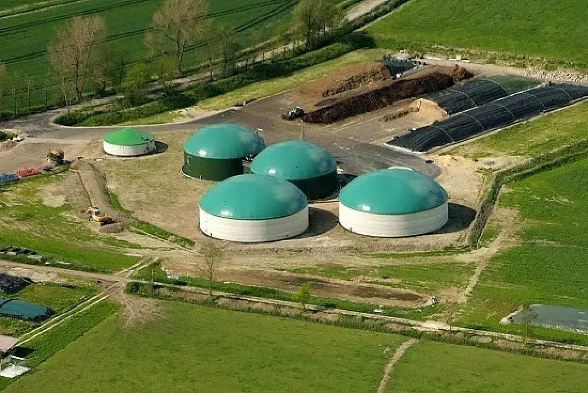 Impianto di biogas con grandi serbatoi verdi e bianchi, circondato da campi verdi. Un esempio di come gli incentivi biogas supportano l'energia rinnovabile.